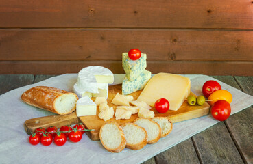 Various types of cheese, tomatoes and baguette on rustic wooden table.