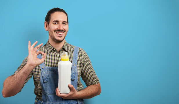 Sustainable Farming. Happy Smiling Young Male Farmer With Eco Fertilizer Bottle Mockup Gives Ok Over Blue Backgorund With Copy Space