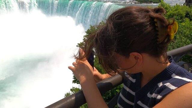 A young woman taking pictures of a breathtaking beauty of cascading water.