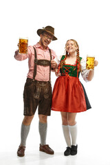 Two celebrating friends. Full lenght portrait of smiling man and woman wearing folk festival outfits, with Bavarian beer glasses. - obrazy, fototapety, plakaty