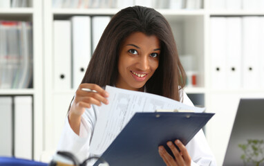 Beautiful black smiling female doctor hold clipboard pad and fill something with silver pen. Physical illness prevention prescribe remedy ward round therapeutist assistance healthy lifestyle concept