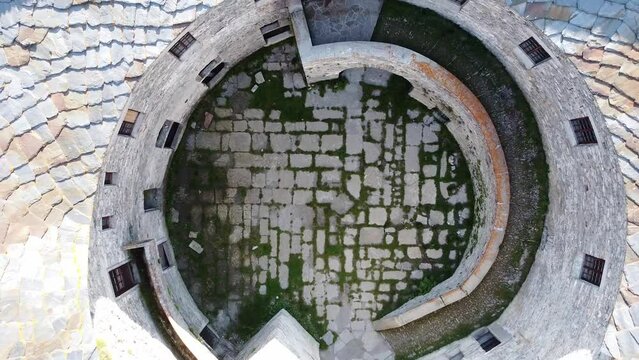 Aerial drone view of paved courtyard of round fortification called Fort de Ronce, Val Cenis, Savoie, Rhone Alpes, France. Bird eye view of old military fort in French Alps, overgrown with green grass