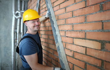 Portrait of constructor making brick wall smooth in order to plastering brick wall. Smiling construction master wearing protective outfit to prevent any trauma. Building concept