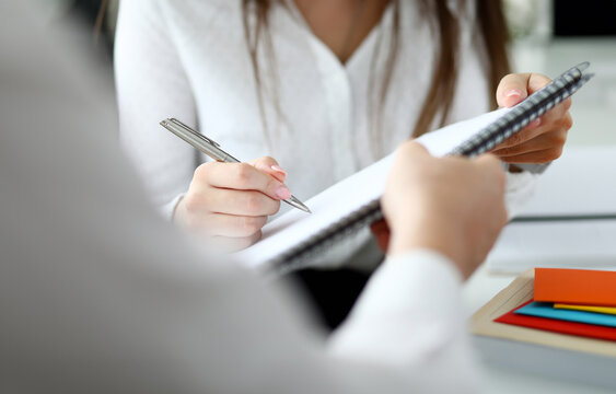 Close-up of people sitting in office and writing something in important document with tender female hands. Smart businessman holding paper folder. Blurred background