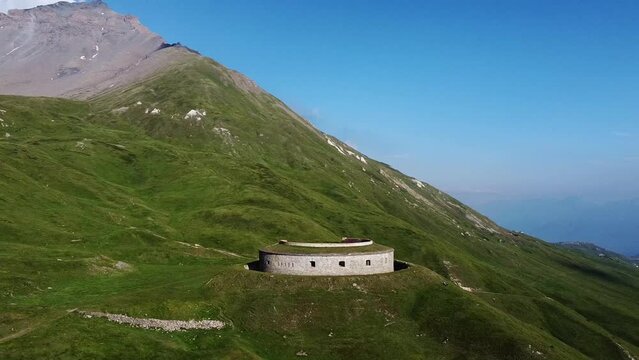 Panoramic aerial drone view of round fortification called Fort de Ronce, Alps mountains and Mont Cenis lake, Val Cenis, Savoie, France. Bird eye view of old military fort overgrown with green grass 