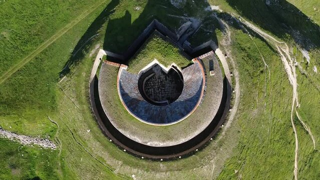 Aerial drone view of round fort called Fort de Ronce, Val Cenis, Savoie, Rhone Alpes, France. Bird eye panoramic view of old military fortification in French Alps, overgrown with bright green grass