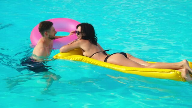 Aerial view of young woman and woman relaxing on inflatable ring in resort pool. Couple enjoying holidays at luxury resort.