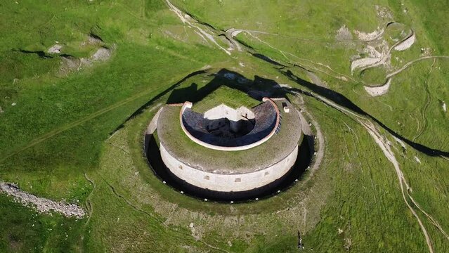 Aerial drone view of round fort called Fort de Ronce, Val Cenis, Savoie, Rhone Alpes, France. Bird eye panoramic view of old military fortification in French Alps, overgrown with bright green grass