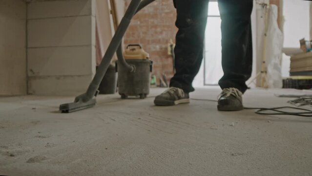 Unrecognizable builder cleaning concrete floor from dust using construction vacuum cleaner