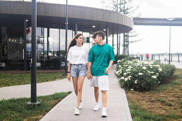 two young people are walking and talking in a city coastal park