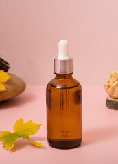 Glass dropper bottle with cosmetics oil or serum at autumn scene composition with podium