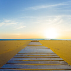 Obraz na płótnie Canvas sandy sea beach with small wooden road at the sunset