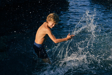 Cheerful boy having fun with splashing water in sea