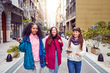 portrait multiracial group of three young women walking down the street happy holding smartphones