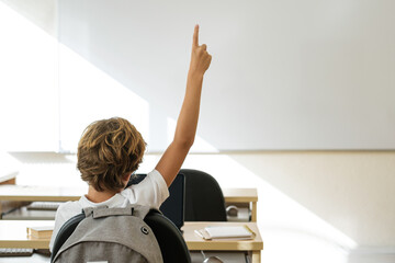 Schoolboy putting hand up in classroom at school