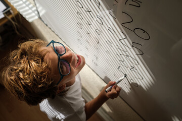 Happy schoolkid writing on whiteboard during math lesson - obrazy, fototapety, plakaty