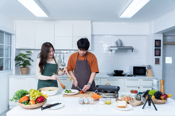 Happy portrait of loving young asian of having fun standing a cheerful preparing food and enjoy cook cooking with vegetables, meat, bread while standing on a kitchen Condo life or home