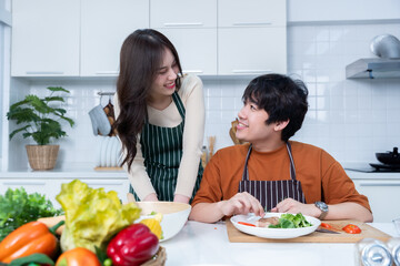 Happy portrait of loving young asian of having fun standing a cheerful preparing food and enjoy cook cooking with vegetables, meat, bread while standing on a kitchen Condo life or home