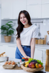 Obraz na płótnie Canvas Happy portrait of young woman asian holding a basket of vegetables of standing a cheerful preparing food and enjoy cook cooking with vegetables, while standing on a kitchen Condo life or home