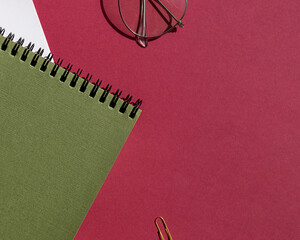 Green spiral notebook with white note paper, pen and glasses on the purple background. Copy space