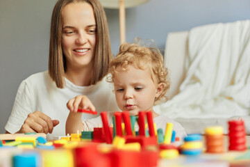 Obraz na płótnie Canvas Babysitter's playful care. Exploring together in the nursery. Happy family leisure time. Joyful mother playing with little baby daughter engaged in game activity at home interior