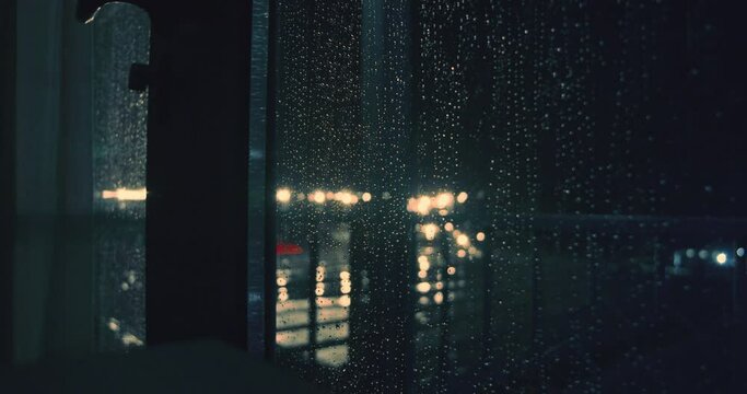 Window with rain drops and dehind heavy rain in night on the street light lamps in rainy season