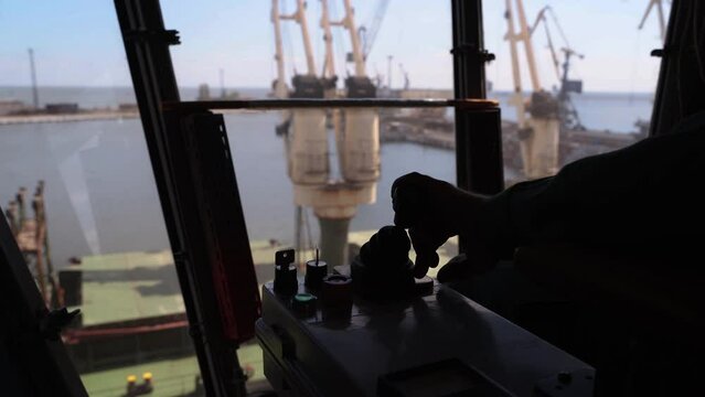 Man hands control joysticks at grain terminal operator cabin workplace. Worker controlling loading grain with arm lever handle from silo to bulker ship via moving trunk machine in dock.