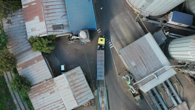 Aerial view from above of grain lorry or dump truck driving through the industrial area of grain elevator silos. Top view of emty body trailer driving along the road. Air drone copter footage.