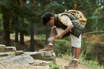 Boy protecting himself from insects using spray during his hiking in the forest - Powered by Adobe