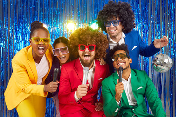 Funny group of young people singing into microphones at a party, dressed in bright costumes,...