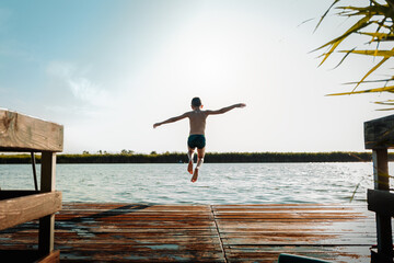 Young boy having fun enjoying a summer day jumping at the lake.