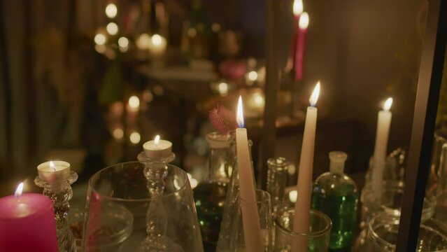 Close up shot of burning candles in candlesticks, vials of potions and other equipment in seers studio in dark colors
