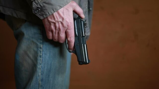An unidentified man in dirty clothes approaches with a 9mm pistol in his hand and cocks it.