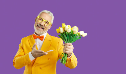 This one's for you, dear. Happy man holding fresh spring flowers. Studio shot of handsome bearded senior gentleman in bright yellow suit, bow tie and glasses smiling and offering you bouquet of tulips