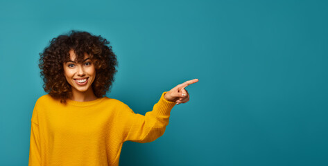 Woman in yellow sweater pointing to the side with her hand and smiling.