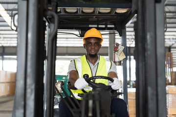 African American male warehouse worker in safety vest and helmet driving and operating on forklift truck for transfer products or parcel goods in the industrial storage warehouse. multicultural worker