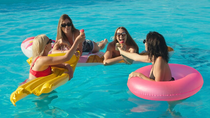 A group of beautiful, young women are eating strawberry popsicles and having fun in the pool.