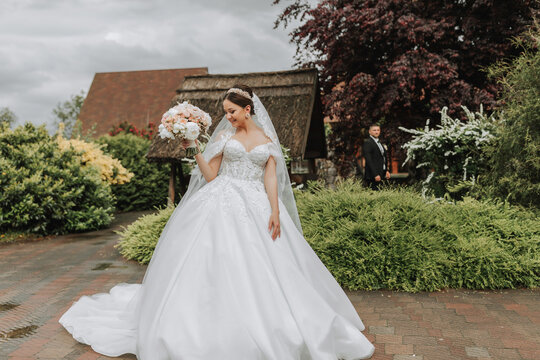 Portrait of a beautiful bride in a white wedding dress with a long train with a modern hairstyle and a veil walking in the garden. Wedding concept