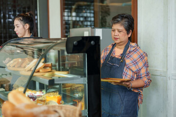 Veteran Asian mother works waitress in daughter cafe, owner daughter works barista making coffee for customers who visit cafe, mother walked out county serve food, daughter came check bakery.