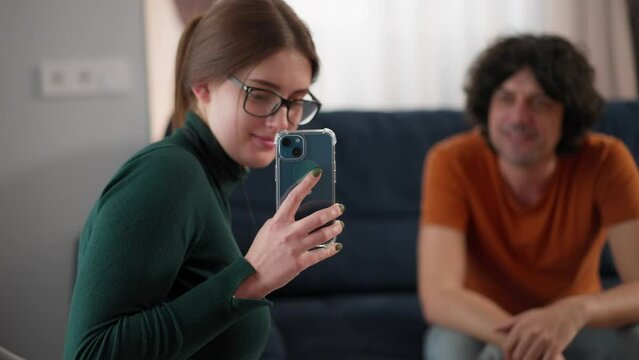 young attractive woman in eyeglasses making selfie at room with handsome man. woman taking photo using phone