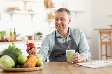 Mature man with glass of fresh smoothie and fruits in kitchen