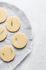 Top view of cut out raw rosemary sugar cookie dough, rosemary cookie dough about to be baked, process of making rosemary sugar cookies