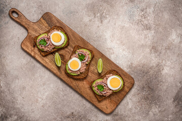 Sandwich with tuna, avocado and boiled egg on a wooden board. Top view, flat lay.