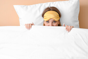 Young woman with sleeping mask, pillow and blanket on beige background