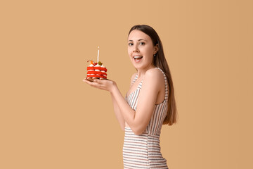Happy young woman with tasty birthday cake on beige background