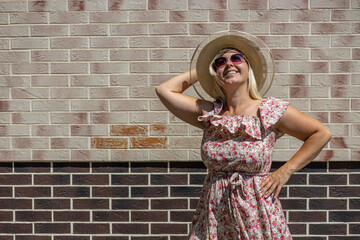 Smiling woman in a beautiful summer sundress looks up against the background of a brick wall. Summer in the city, on a textural background. Sweet woman is happy with the onset of summer.