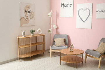 Interior of living room with cozy grey armchairs, coffee table, shelving unit and different paintings