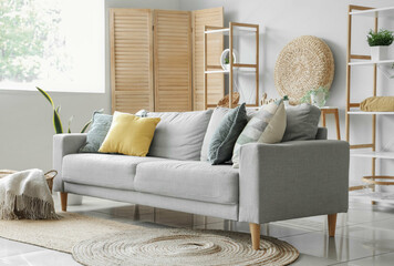 Cozy grey sofa and basket with soft blanket in interior of light living room