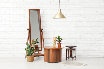 Brown wooden coffee tables with floor mirror and houseplants near white brick wall