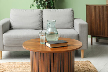 Brown wooden coffee table with jug of water and book near couch in living room